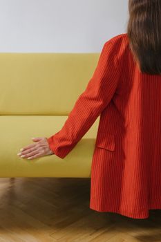 室内黄色沙发上坐着一位穿红色外套的女人，从后面看过去
