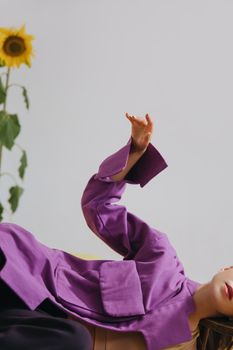 一个女人穿着紫色外套，躺在向日葵旁，举起了手臂