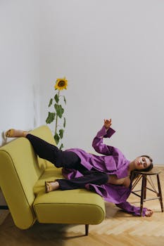 一位身着紫色衣服的女子，在室内一张时尚沙发上闲坐，背景是向日葵