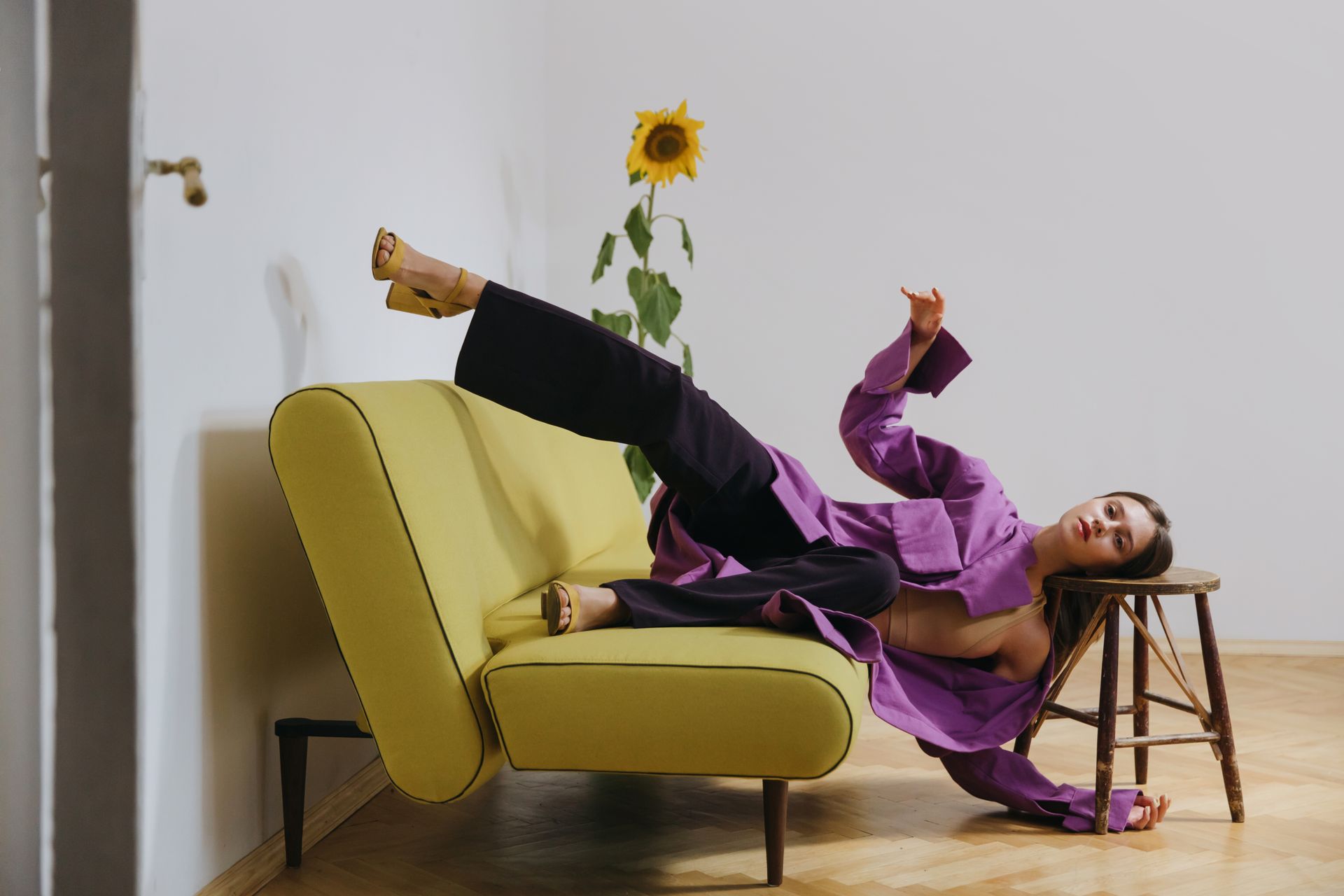 Woman in Purple Coat and Black Slocks lying on a Yellow Sofa