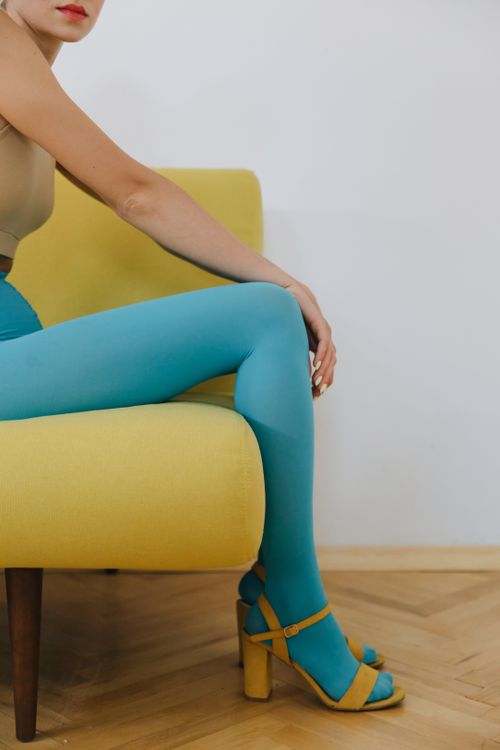 Free A stylish woman in blue tights and sandals sitting on a yellow chair in a minimalistic setting. Stock Photo
