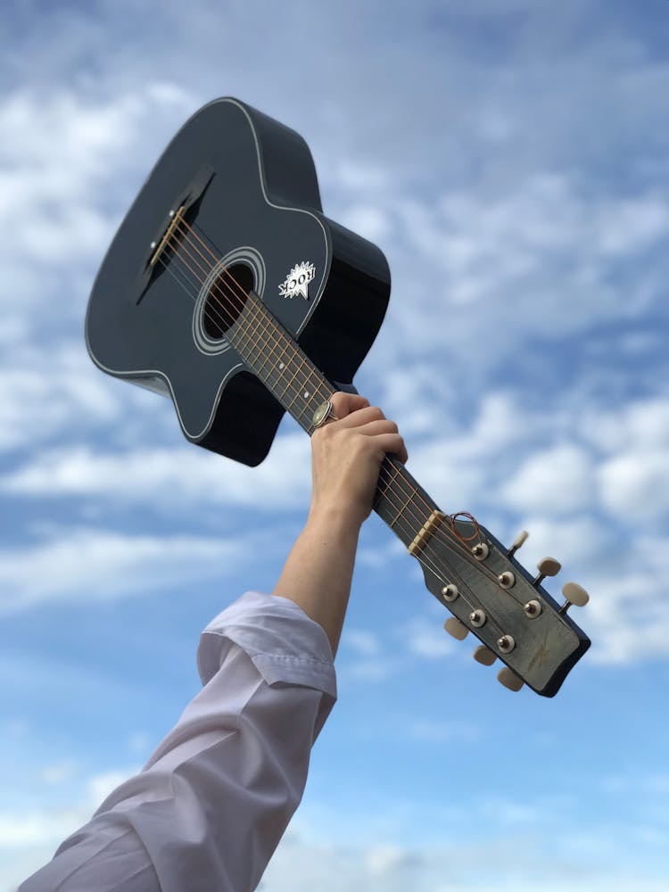 Person Raising A Black Acoustic Guitar