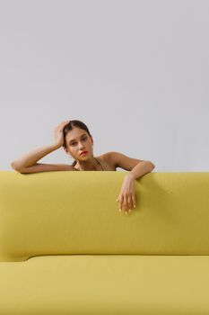 一位时尚的成年女性坐在充满活力的黄色沙发上，背景简约