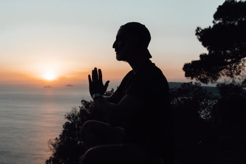 Silhouette of meditating man sitting on seacoast at sundown