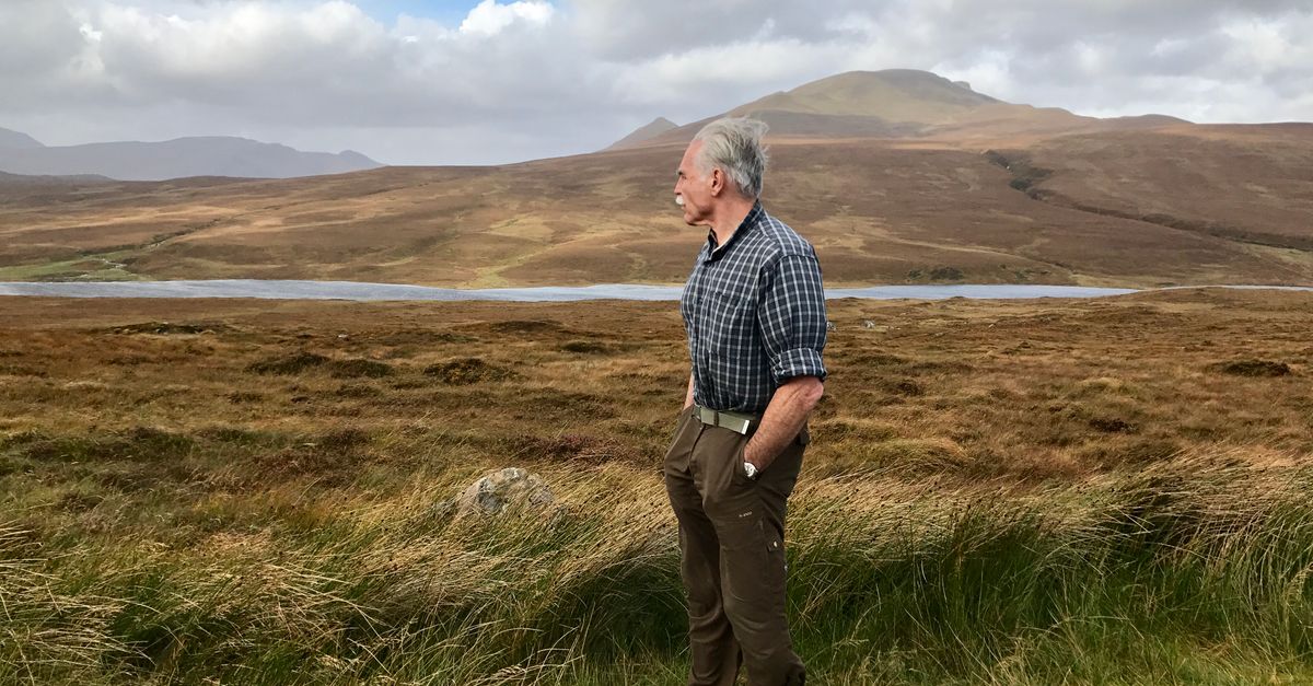 pastor in hoodie standing on a cliff in the Scottish Highlands, wind blowing, looking contemplative