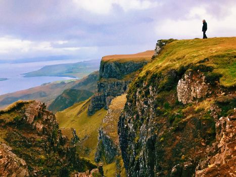 Lone traveler standing atop a rugged cliff with expansive coastal views.
