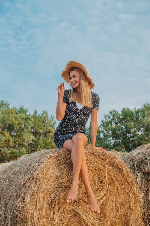 Cheerful woman sitting on haystack in field