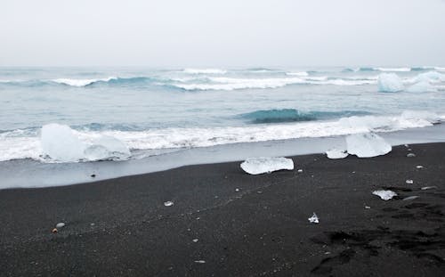 Amazing scenery of powerful waving ocean with black sandy beach and crystal glaciers in Jokulsarlon lagoon in Iceland