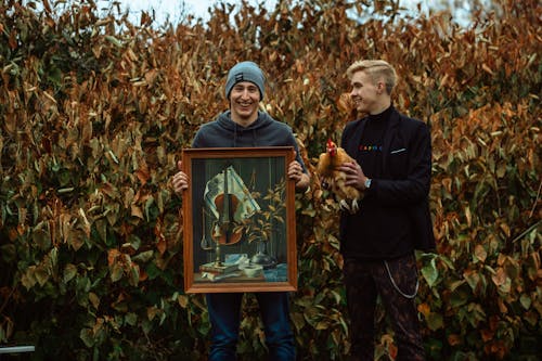 Man Holding a Frame Beside Man Holding a Rooster