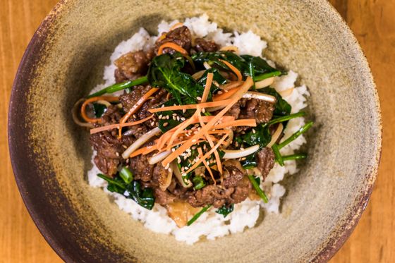 Ceramic bowl of white rice topped with sweet soy beef, wilted spinach, carrot strips and sesame