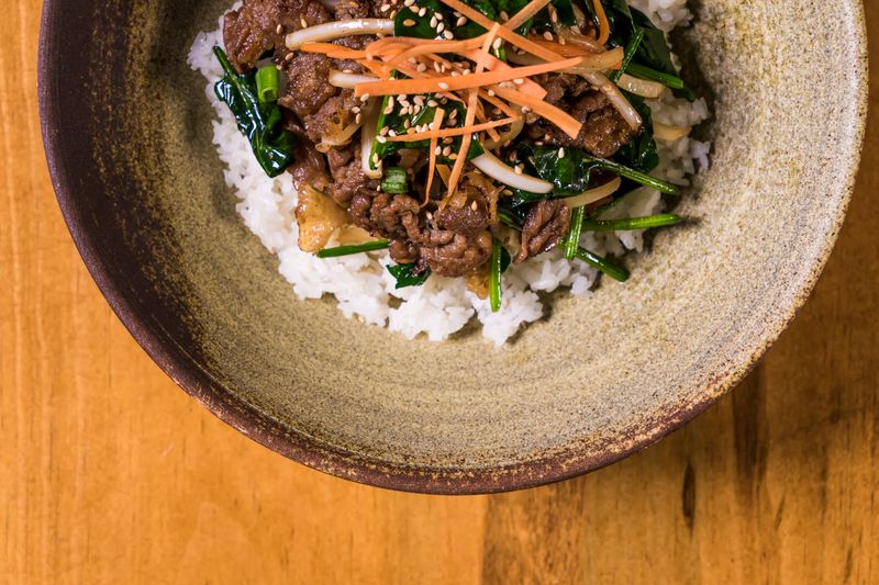 Korean beef bowl with stir-fried beef and fresh vegetables over rice in a rustic bowl