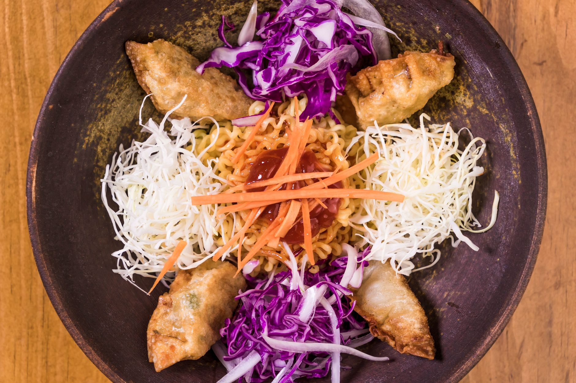 Top view of a colorful Korean noodle bowl with dumplings, cabbage, and carrot garnish.