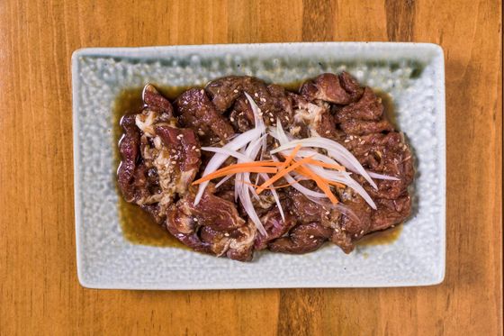 Rectangular plate of glossy soy glazed sliced beef topped with thin white onion and carrot strips