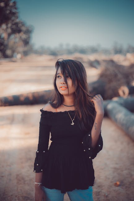 Young woman in an off-shoulder top posing outdoors with a confident expression.
