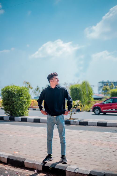Free Confident man in black hoodie and jeans posing on sunny sidewalk. Stock Photo