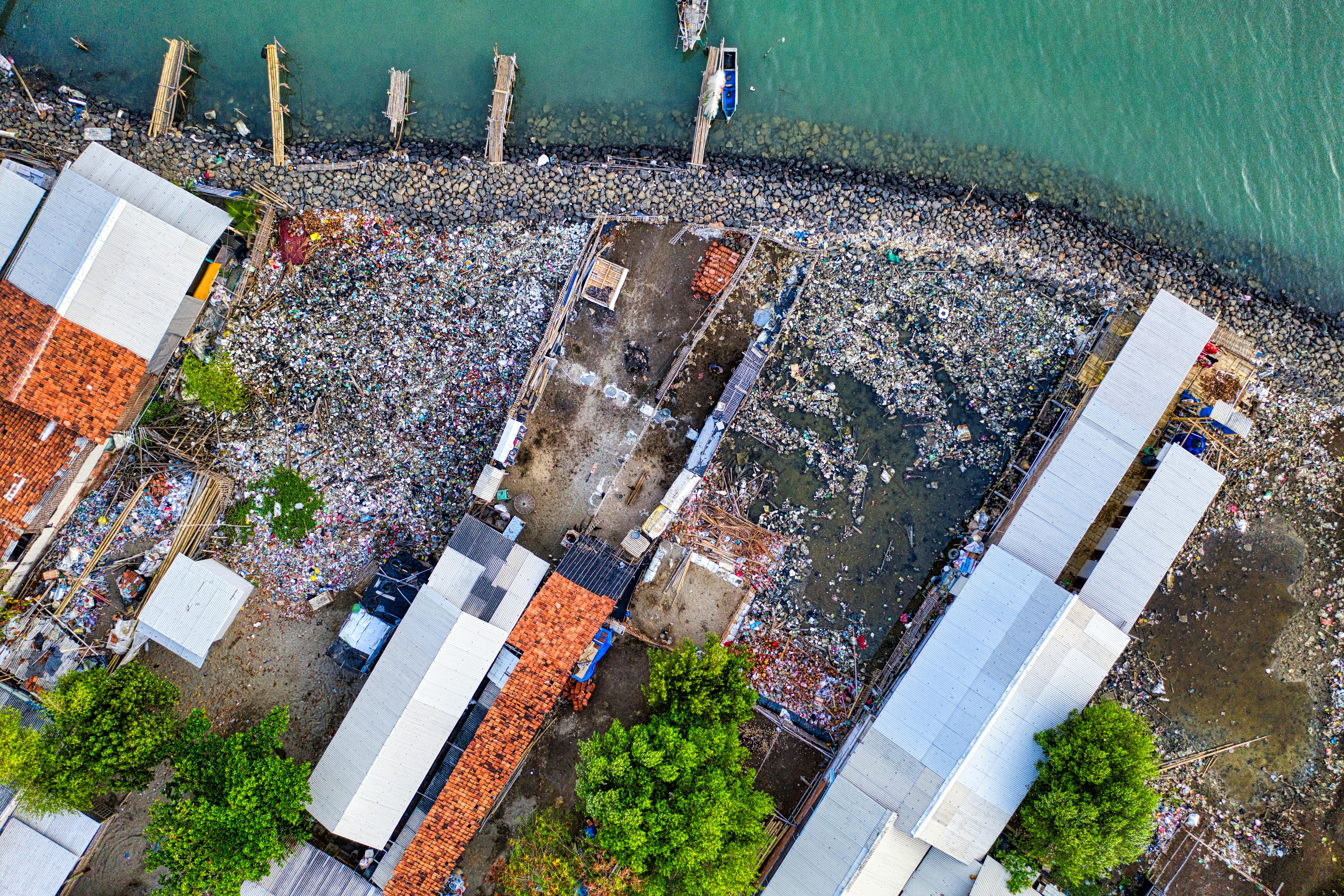 Aerial view of house roofs on ocean coast with docks and moored boats in summer harbor