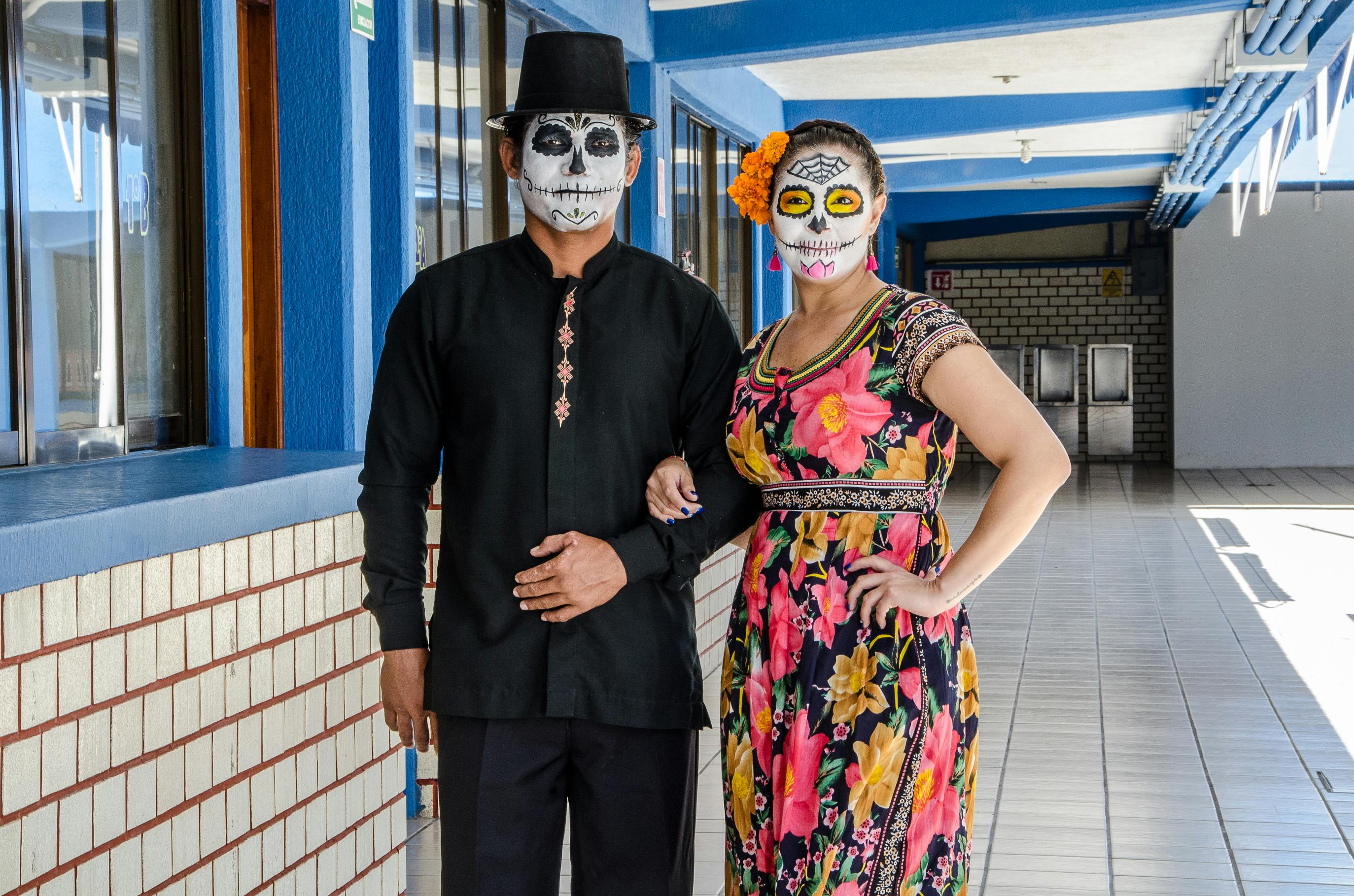 A couple in traditional Day of the Dead costumes posing indoors with face paint.