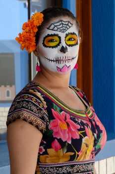 Vibrant portrait of a woman in Dia de los Muertos makeup with floral dress and orange flowers.