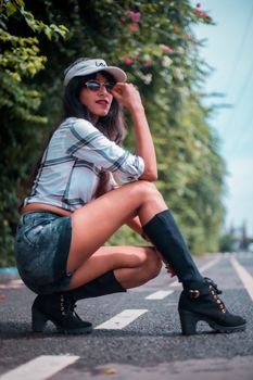 Stylish woman in denim shorts and plaid shirt posing confidently on a sunny road.