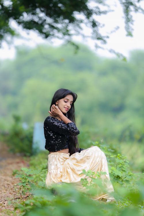 Free A young woman in a long skirt sits peacefully outdoors, surrounded by lush greenery. Stock Photo