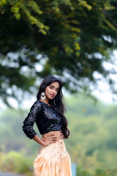 Free Elegant woman posing outdoors with fashionable attire under a lush tree. Stock Photo