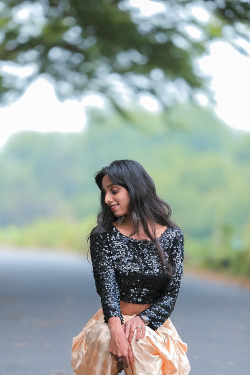 Free Portrait of a woman in a black sequin blouse smiling against a lush outdoor backdrop. Stock Photo