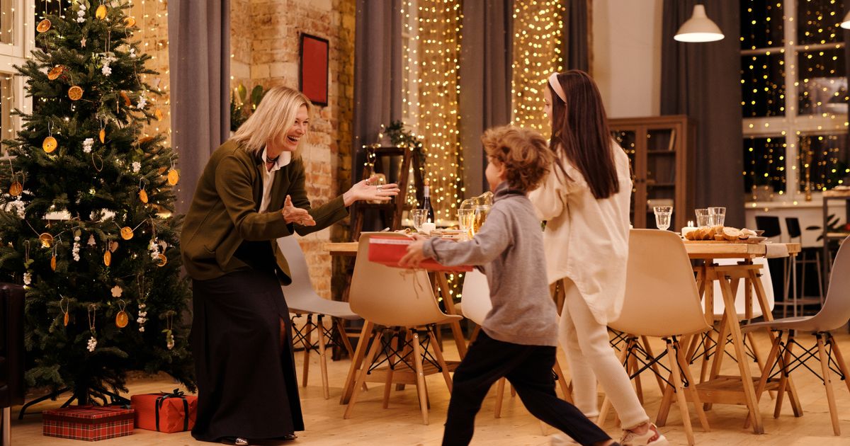 Two children presenting wrapped gifts to their smiling mother in a warm home setting