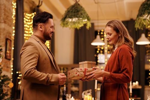 Free Joyful couple exchanging gifts in a festive indoor setting, capturing the warm spirit of the holiday season. Stock Photo