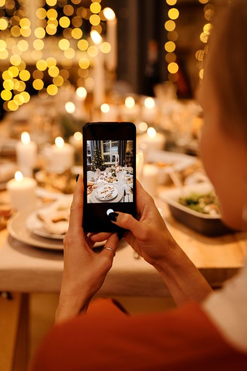 Free Woman photographing a holiday dinner table with festive lights indoors. Stock Photo