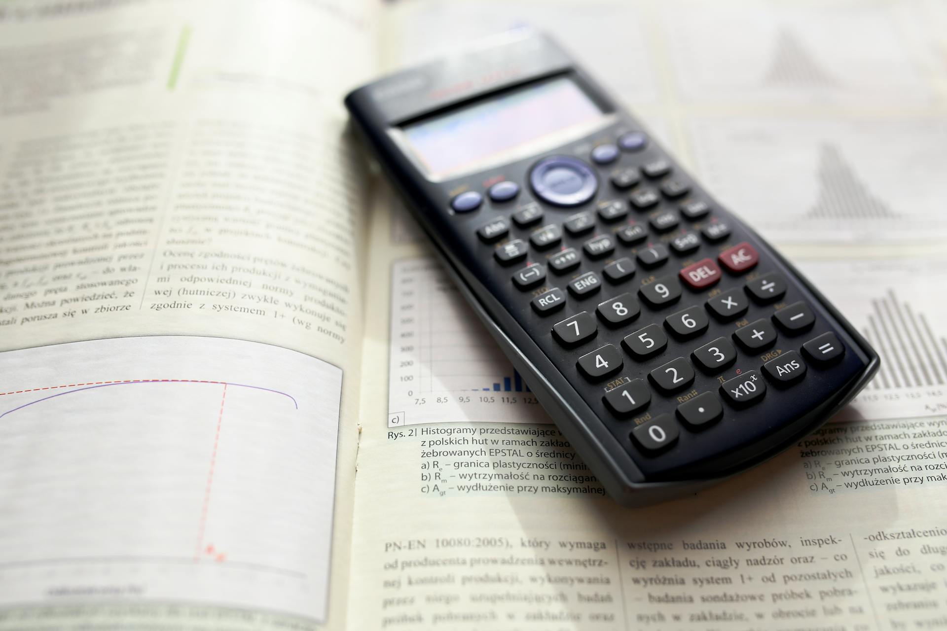 A graphing calculator rests on an open mathematics book with graphs and equations.