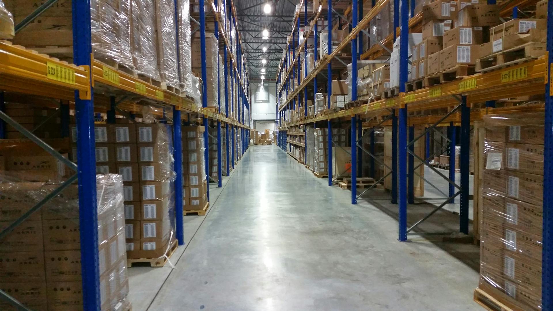 Interior view of a large warehouse aisle lined with stacks of organized cardboard boxes.