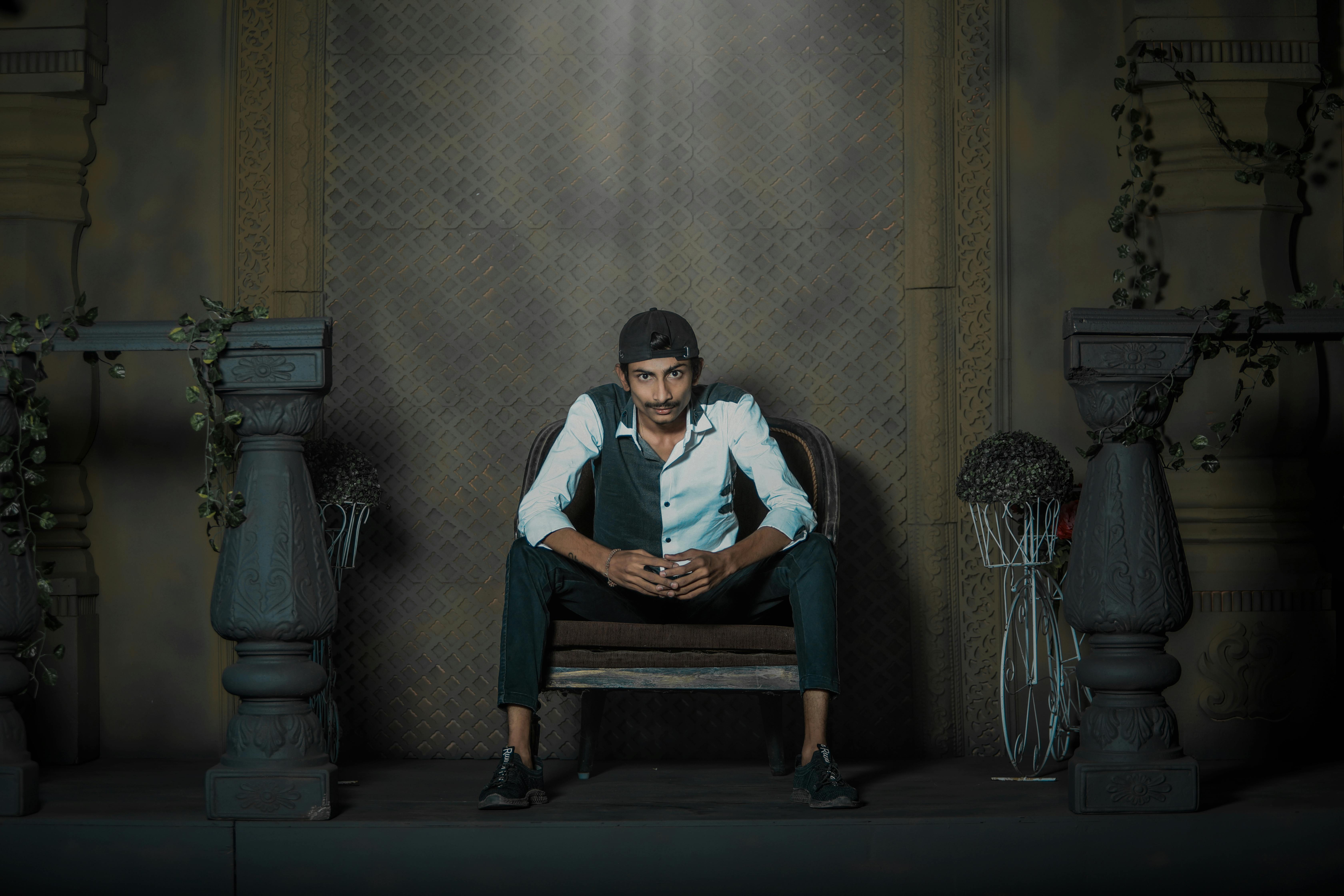 Young man sitting on a chair in moody lighting, indoors with ornate decor.