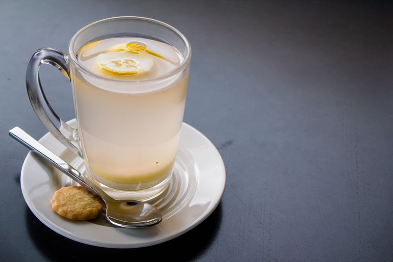 Refreshing lemon infused water in clear glass with biscuit and saucer, perfect for a health-focused lifestyle.