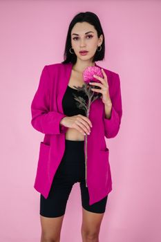 一位身着粉色西装外套的女性肖像，手持一朵花，背景与之相配