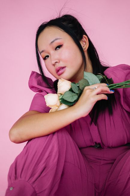 Stylish portrait of an Asian woman holding flowers against a pink background.