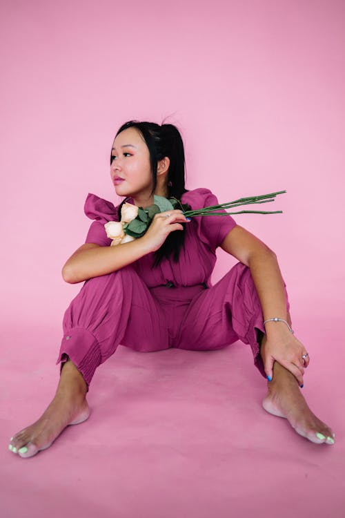 A Woman in Purple Jumpsuit Sitting on the Floor while Holding Flowers