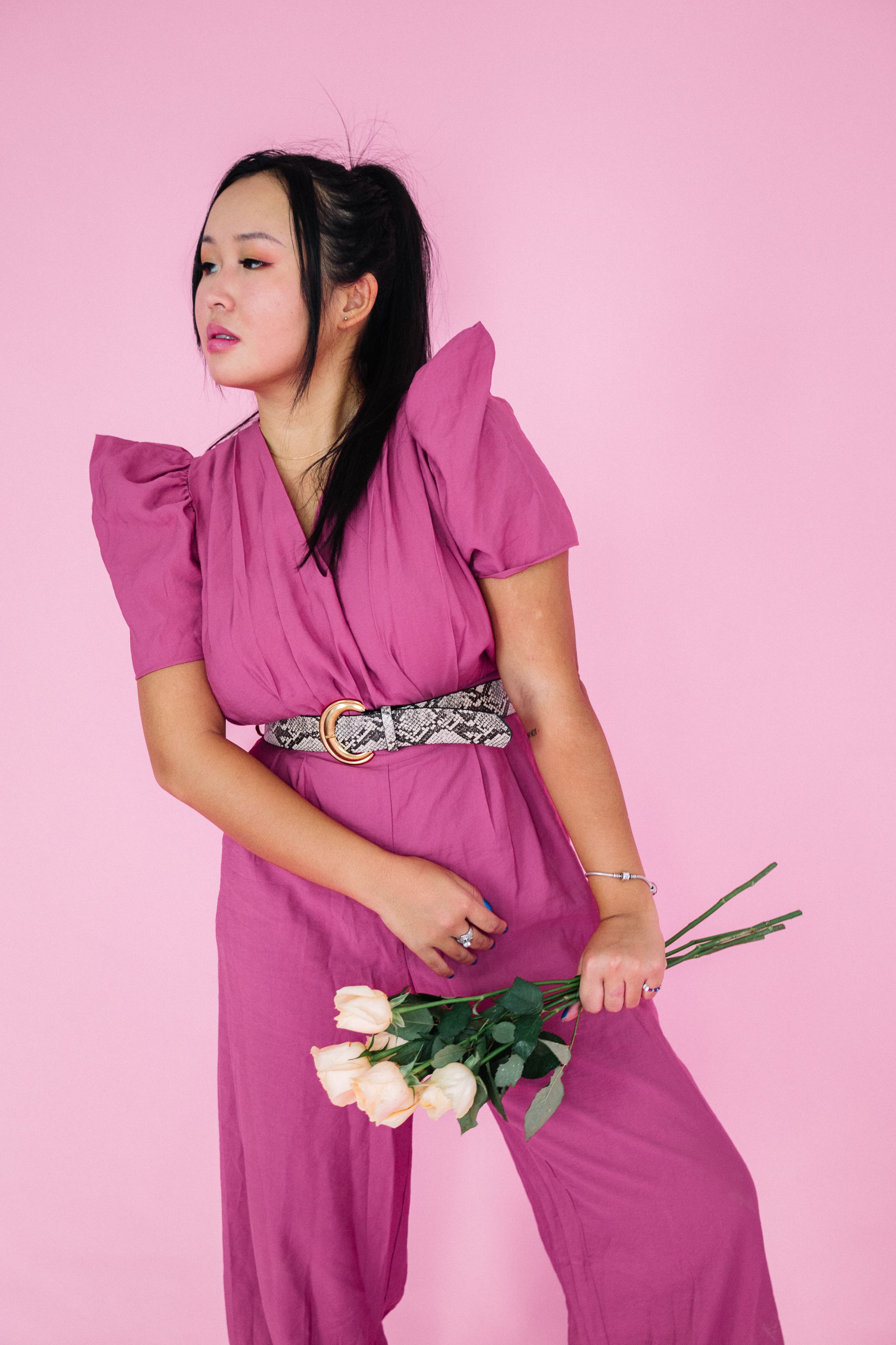 优雅的女人身着紫色衣服，手持玫瑰，站在粉红色背景前