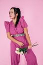 优雅的女人身着紫色衣服，手持玫瑰，站在粉红色背景前