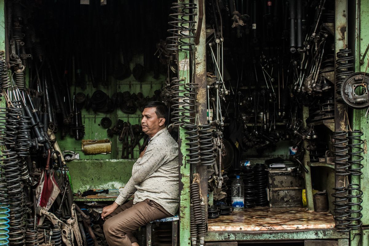A trader sitting in a small stall packed with springs and suspension parts