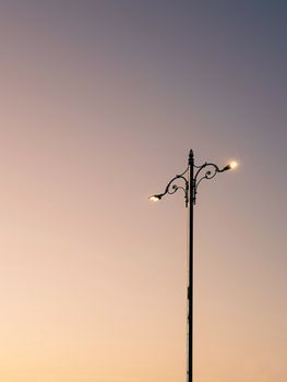 A vintage street lamp glowing softly against a pastel dawn sky with an elegant design.