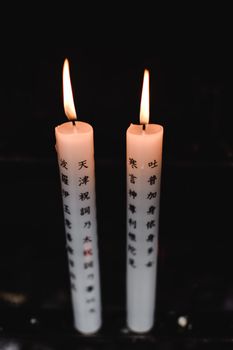 在京都寺庙的暗色背景下，两支点燃的蜡烛映衬着日本汉字