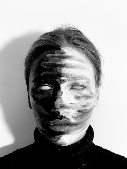 Black and white of young young scary female with contrast paints on face and blank eyes in light studio