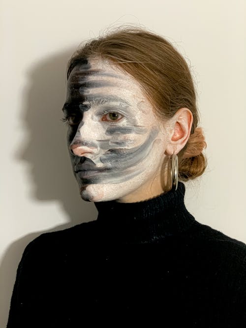 Young ponder woman with painted face looking away in white studio