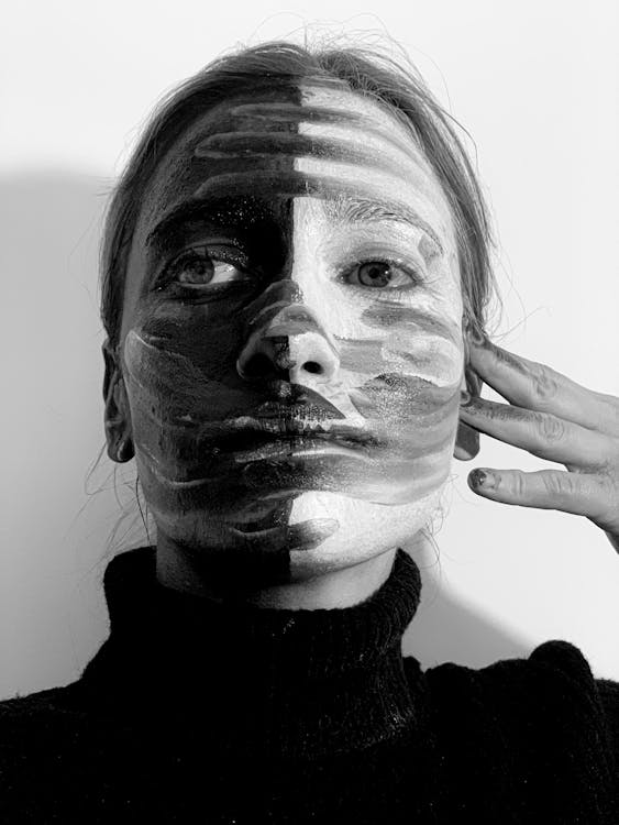 Free Black and whit of calm young lady applying contrast paints on face and looking away Stock Photo