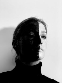 Black and white from below of weird female with greasepaint on face looking away while standing on white background with closed eye