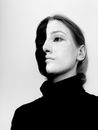 Black and white from below of spooky female with paints on face wearing turtleneck looking away while standing against white background