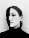 Black and white of strange enigmatic female in pullover with paints on face looking away while standing against white background