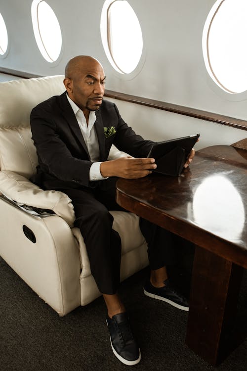A Man in a Black Suit Using a Tablet in an Airplane