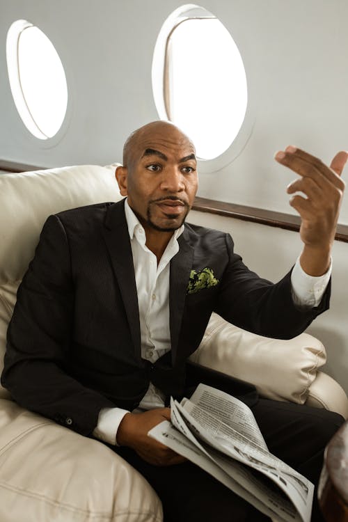 A Man in a Black Suit Holding a Newspaper while Sitting in an Airplane