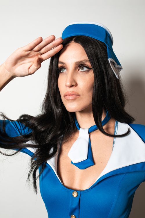 Free Elegant flight attendant in blue uniform making a salute gesture indoors. Stock Photo